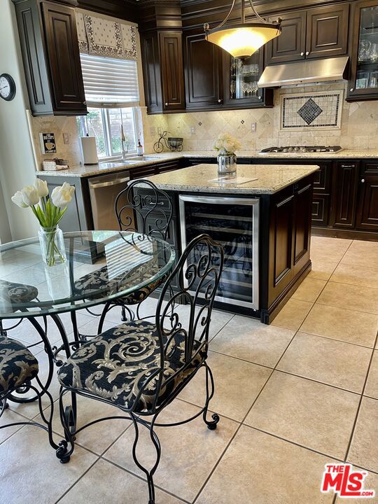 kitchen featuring wine cooler, light stone countertops, dark brown cabinetry, and appliances with stainless steel finishes