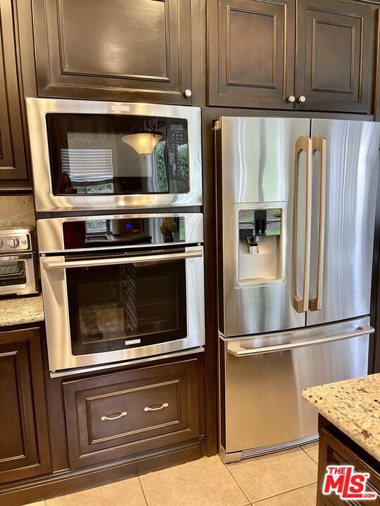 kitchen featuring light stone countertops, appliances with stainless steel finishes, light tile patterned floors, and dark brown cabinets