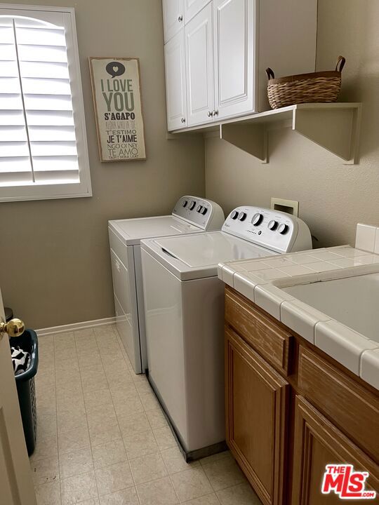 clothes washing area with cabinets and washer and clothes dryer