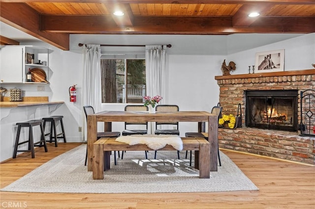 dining space with a brick fireplace, wooden ceiling, and light wood-type flooring