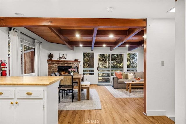 interior space with white cabinetry, beam ceiling, light hardwood / wood-style floors, and a brick fireplace