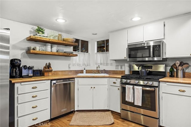 kitchen featuring appliances with stainless steel finishes, sink, light hardwood / wood-style flooring, and white cabinets