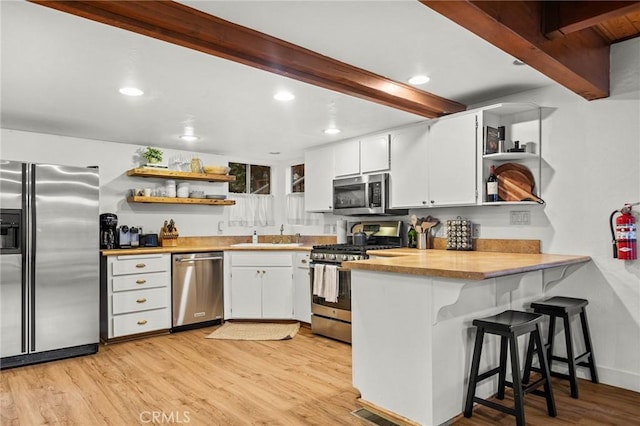 kitchen with white cabinetry, stainless steel appliances, kitchen peninsula, beamed ceiling, and light wood-type flooring