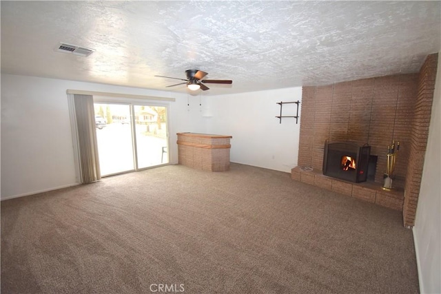 unfurnished living room with ceiling fan, a brick fireplace, carpet, and a textured ceiling