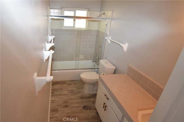 full bathroom featuring hardwood / wood-style flooring, vanity, shower / bath combination with glass door, and toilet