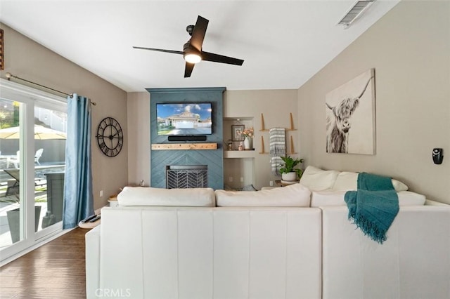 living room featuring ceiling fan, a large fireplace, and dark wood-type flooring