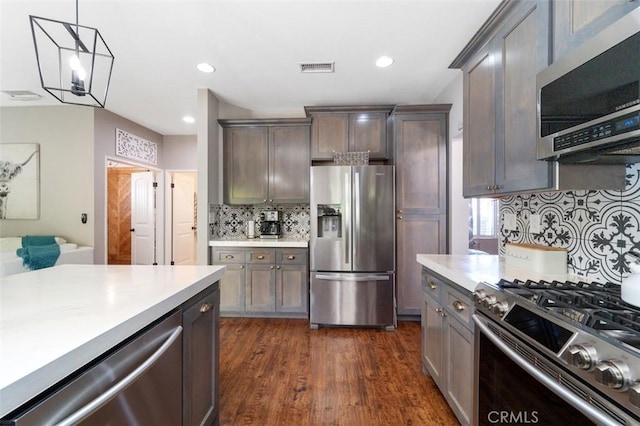 kitchen featuring dark wood-type flooring, hanging light fixtures, a notable chandelier, backsplash, and appliances with stainless steel finishes