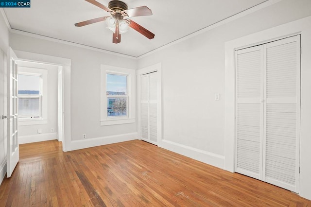 unfurnished bedroom with ceiling fan, hardwood / wood-style floors, crown molding, and multiple closets