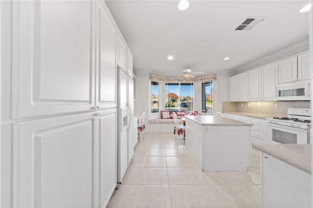 kitchen featuring ceiling fan, light tile patterned floors, a kitchen island, white appliances, and white cabinets