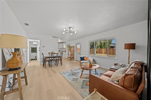 living room featuring a textured ceiling, an inviting chandelier, and light hardwood / wood-style flooring