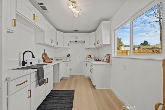 kitchen with white cabinets, light wood-type flooring, and sink