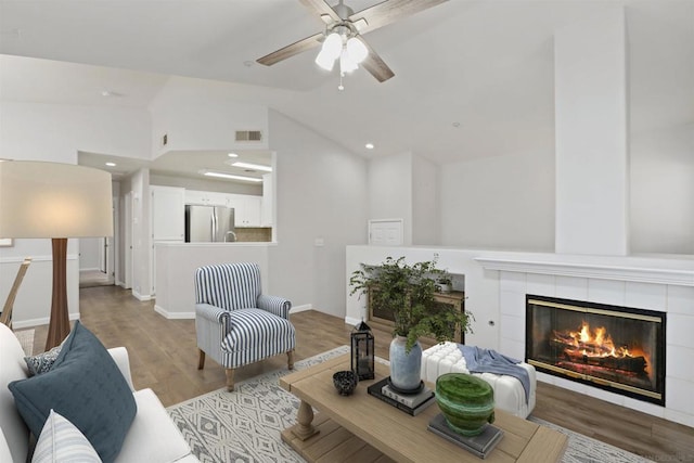 living room with a tile fireplace, light wood-type flooring, high vaulted ceiling, and ceiling fan