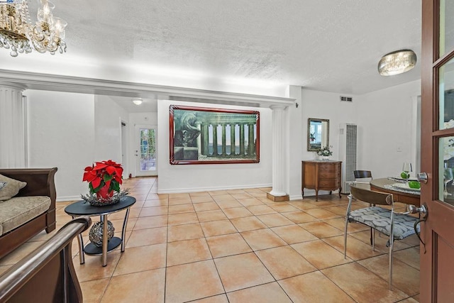 interior space with a textured ceiling, an inviting chandelier, ornate columns, and light tile patterned flooring