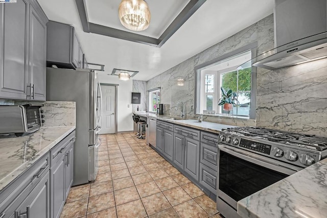 kitchen with gray cabinetry, sink, range hood, and appliances with stainless steel finishes