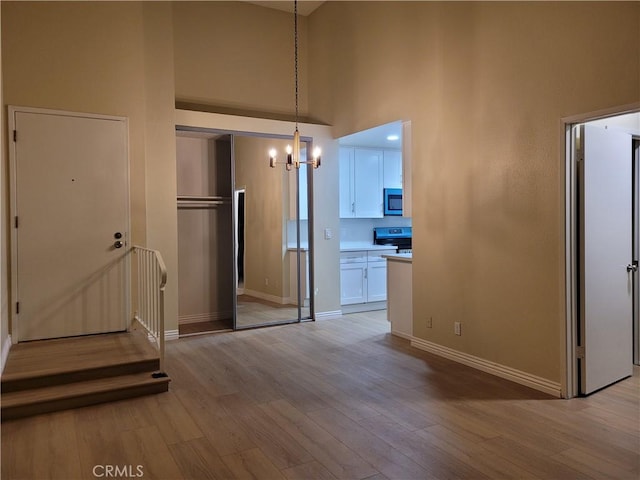 unfurnished dining area with light wood-type flooring, a towering ceiling, and a chandelier