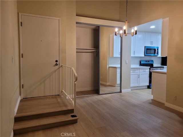 kitchen with white cabinetry, hanging light fixtures, a notable chandelier, black / electric stove, and light hardwood / wood-style floors