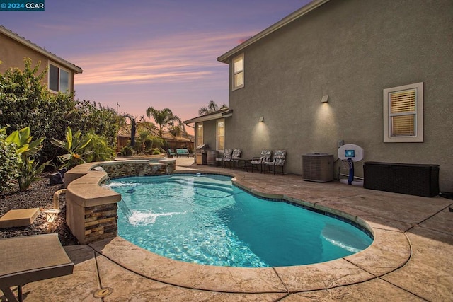 pool at dusk featuring central AC unit, pool water feature, a patio area, and an in ground hot tub