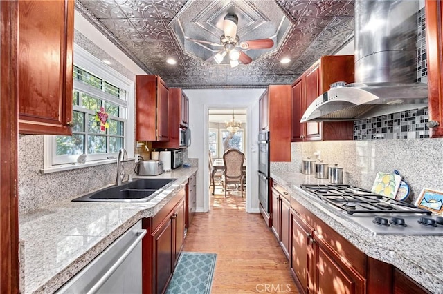 kitchen featuring stainless steel appliances, range hood, ceiling fan with notable chandelier, light hardwood / wood-style flooring, and sink