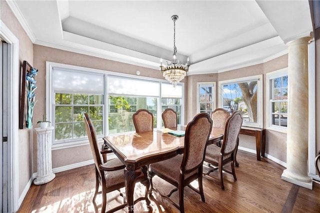 dining space with dark wood-type flooring, a tray ceiling, an inviting chandelier, and decorative columns