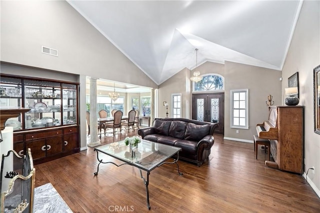 living room with high vaulted ceiling, dark wood-type flooring, an inviting chandelier, and ornate columns