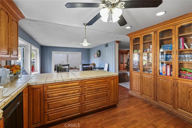 kitchen with tile countertops, kitchen peninsula, dishwasher, wood-type flooring, and a textured ceiling