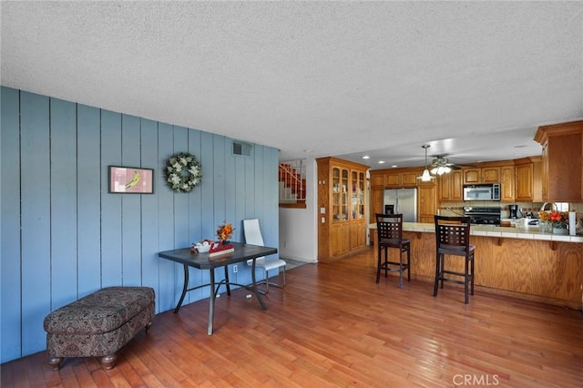 kitchen with light hardwood / wood-style floors, kitchen peninsula, a breakfast bar area, stainless steel appliances, and tile counters