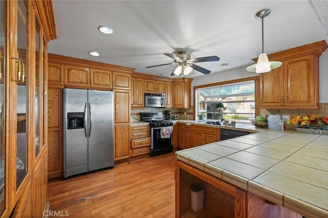 kitchen with decorative backsplash, tile counters, stainless steel appliances, and light wood-type flooring