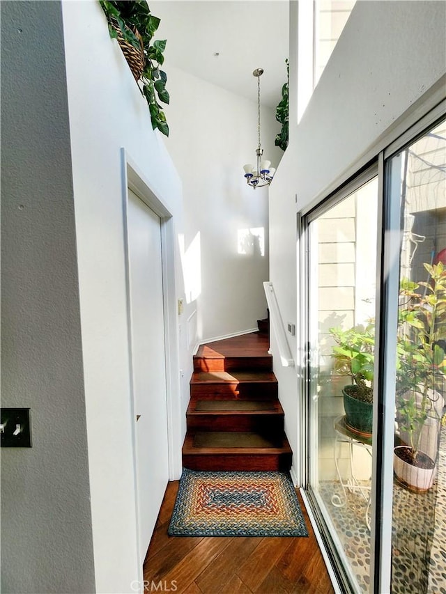 stairway with a high ceiling, wood-type flooring, and a notable chandelier