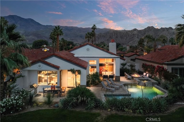 back house at dusk with a mountain view, a swimming pool with hot tub, and a patio area