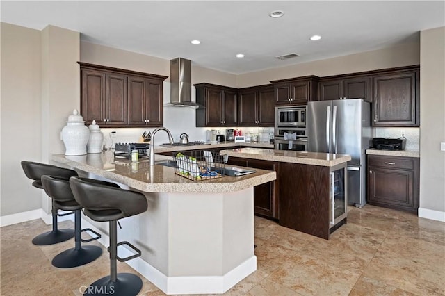 kitchen with kitchen peninsula, a kitchen breakfast bar, dark brown cabinets, stainless steel appliances, and wall chimney range hood