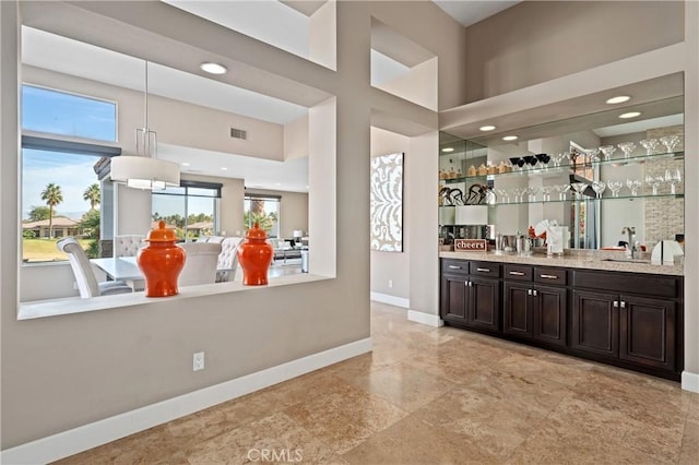 bar featuring dark brown cabinets, light stone counters, pendant lighting, and sink