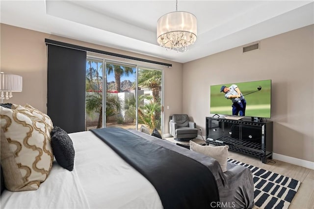 bedroom featuring a notable chandelier, light hardwood / wood-style floors, access to outside, and a tray ceiling