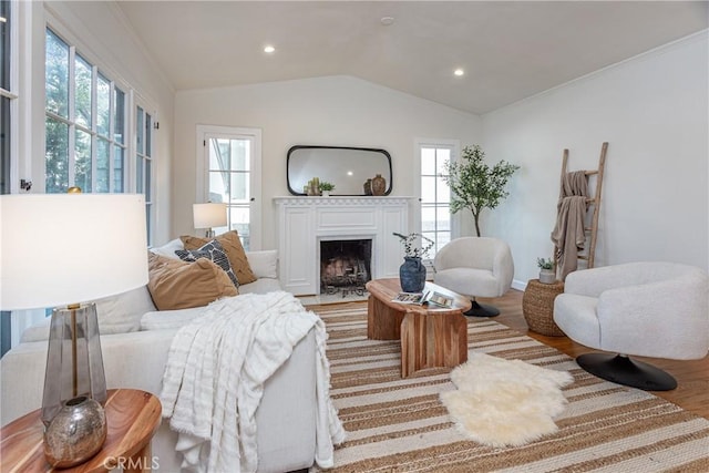 living room featuring light wood-type flooring, vaulted ceiling, plenty of natural light, and ornamental molding