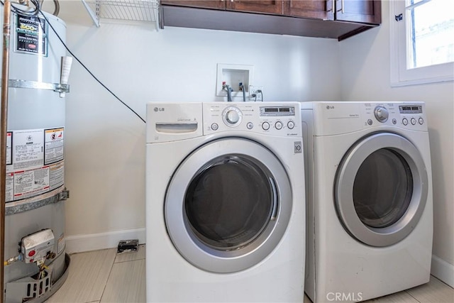 washroom with secured water heater, washing machine and dryer, light tile patterned flooring, and cabinets