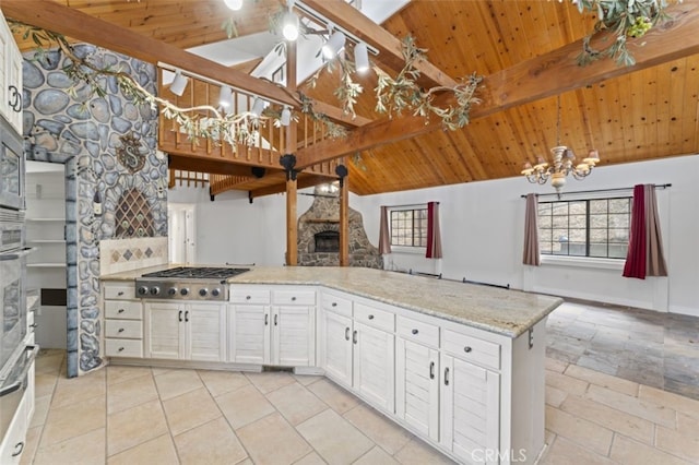 kitchen with stainless steel gas stovetop, wood ceiling, a stone fireplace, beam ceiling, and white cabinets