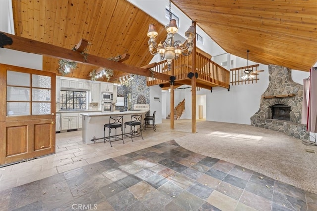 unfurnished living room with light carpet, wood ceiling, a stone fireplace, high vaulted ceiling, and beam ceiling