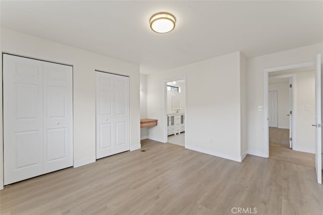 unfurnished bedroom with ensuite bathroom, multiple closets, and light wood-type flooring