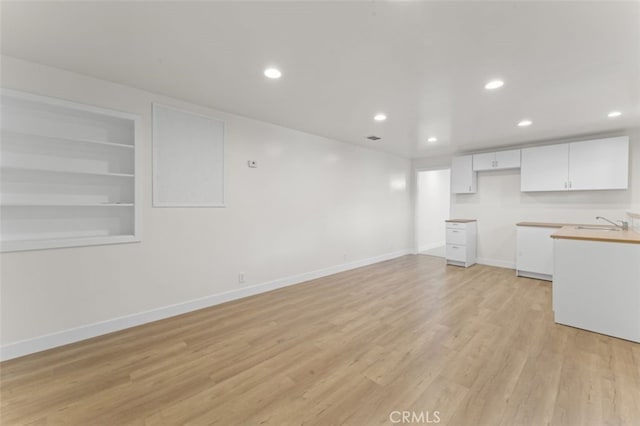 kitchen featuring light wood-type flooring, sink, white cabinets, and built in shelves