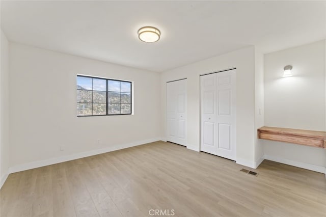 unfurnished bedroom featuring two closets and light hardwood / wood-style flooring