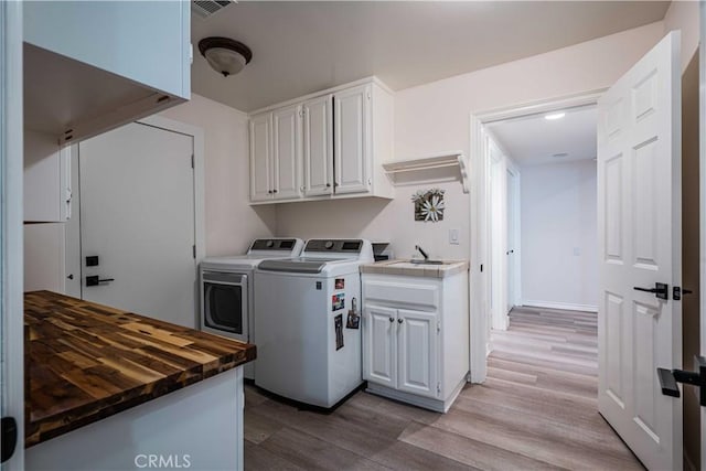 clothes washing area featuring cabinets, sink, washer and dryer, and light wood-type flooring