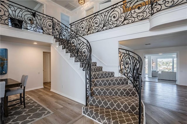 stairway with a towering ceiling, wood-type flooring, and ornamental molding