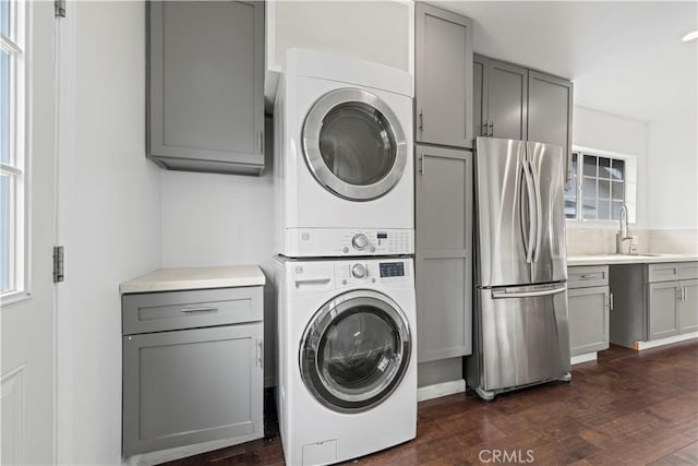 laundry room featuring sink, stacked washer and clothes dryer, and dark hardwood / wood-style flooring