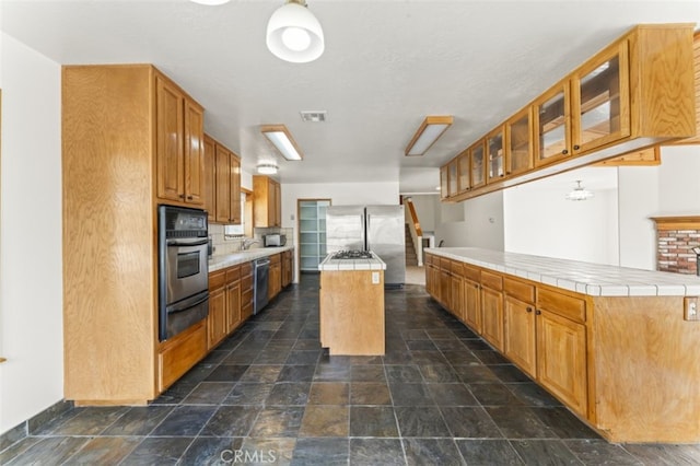 kitchen featuring tile countertops, appliances with stainless steel finishes, backsplash, a center island, and sink