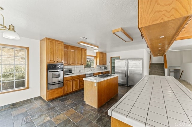 kitchen with appliances with stainless steel finishes, tile counters, tasteful backsplash, a center island, and sink