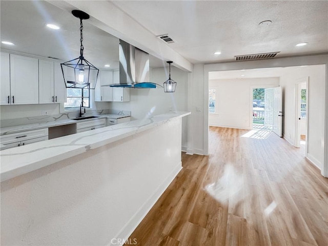 kitchen with island exhaust hood, decorative light fixtures, white cabinets, light stone counters, and sink