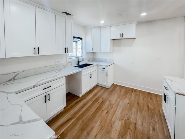 kitchen with sink, light stone counters, and white cabinetry