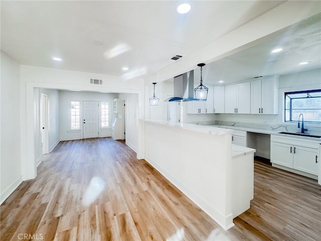 kitchen with white cabinetry, sink, hanging light fixtures, ventilation hood, and light wood-type flooring