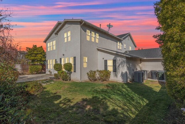 back house at dusk with a lawn, cooling unit, and a patio