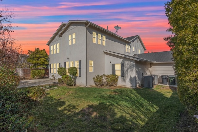 back house at dusk featuring a patio area, cooling unit, and a yard