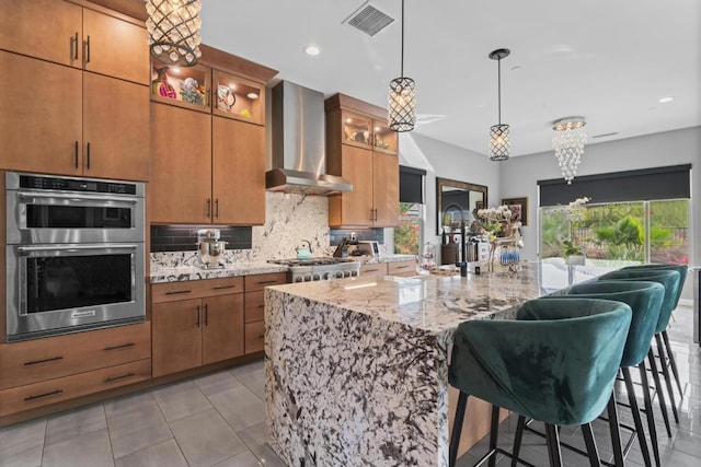 kitchen with light stone countertops, stainless steel appliances, wall chimney range hood, tasteful backsplash, and a kitchen bar